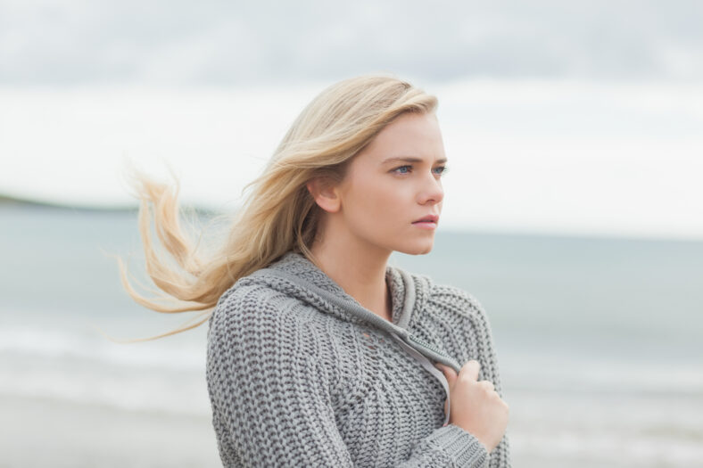 Close up side view of a cute young woman in gray knitted jacket on the beach