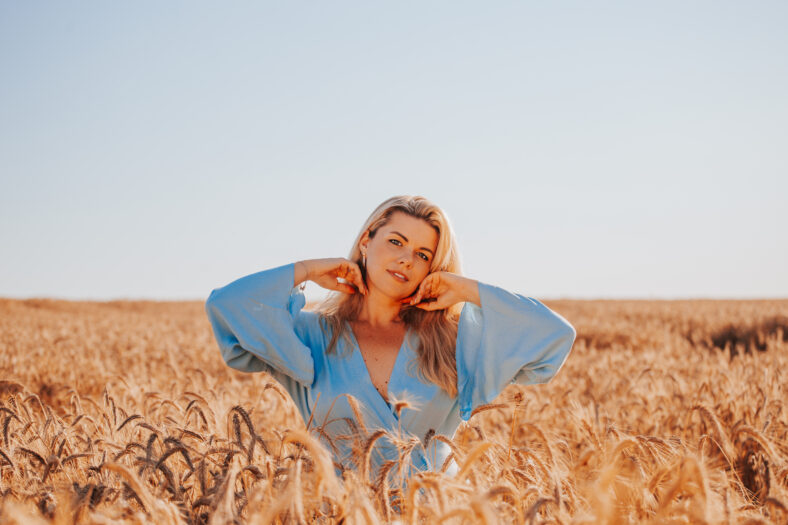 Beautiful adult blonde woman in summer in a field among ears of corn enjoys the warmth and fragrance of flowers - a portrait of a charming beauty