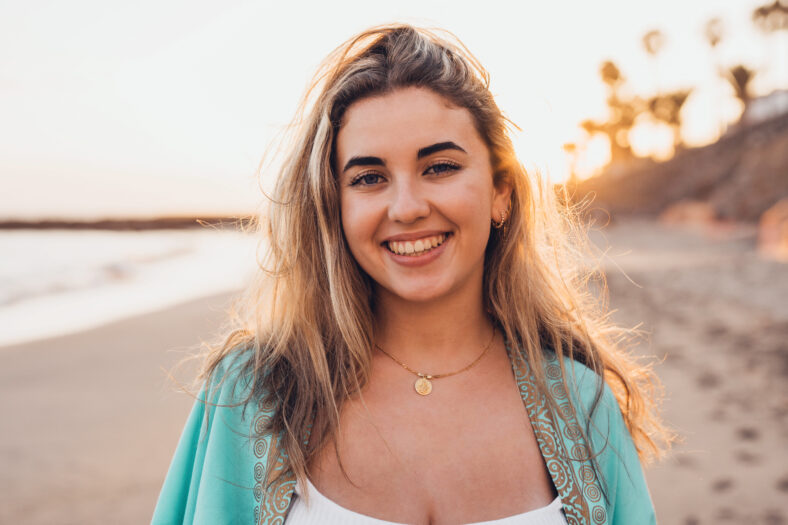 Portrait of one happy beautiful woman on the sand of the beach enjoying and having fun at the sunset of the day. Looking at the camera smiling.