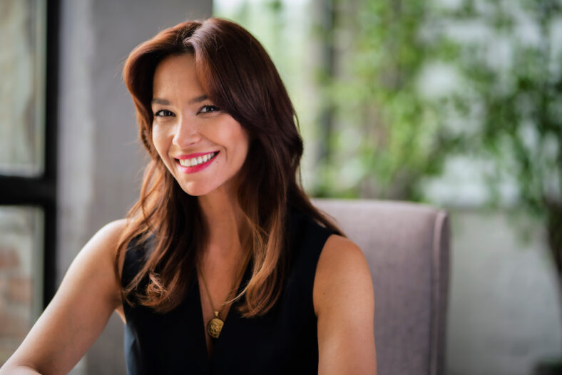 Close-up of a beautiful mid aged woman relaxing in an armchair by the window. Attractive female looking at camera and cheerful smiling.