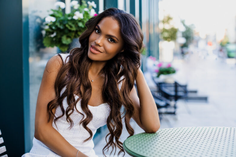 Hermoso retrato de una chica estadounidense con el pelo largo y rizado sentado en un volante en un café. Mujer negra sonriendo al aire libre. Hermosa chica de piel oscura en un café