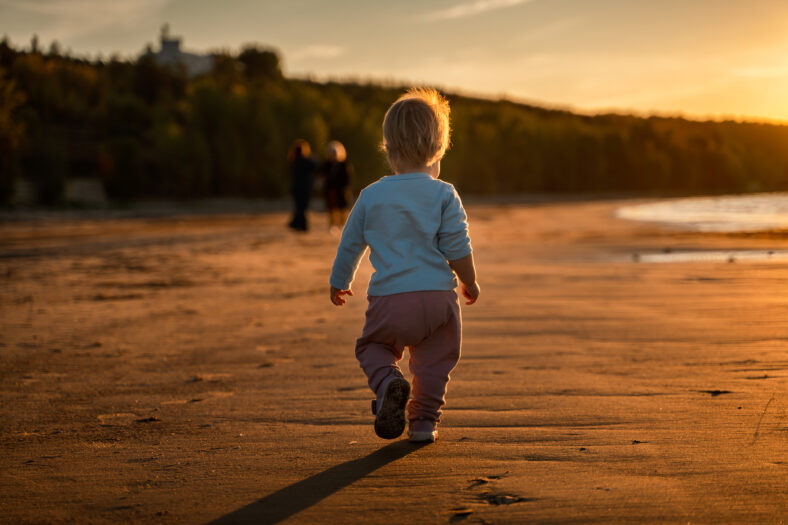 Little baby child toddler walks along an empty beach by the sea at sunset alone, calm and relax, active childhood