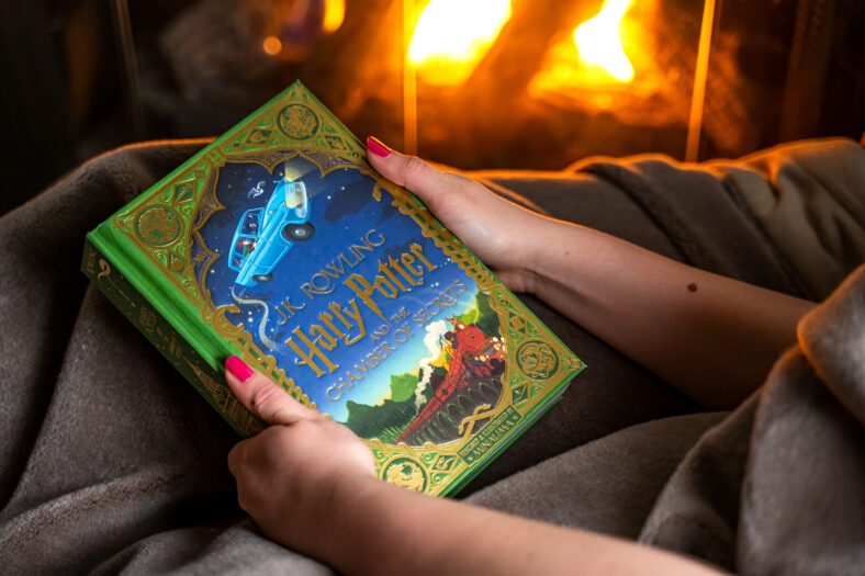 Adolescente leyendo el segundo libro sobre Harry Potter cerca de la chimenea.