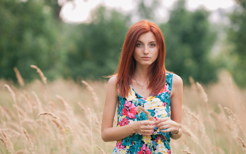 Young  redhead woman in a summer dress posing at meadow