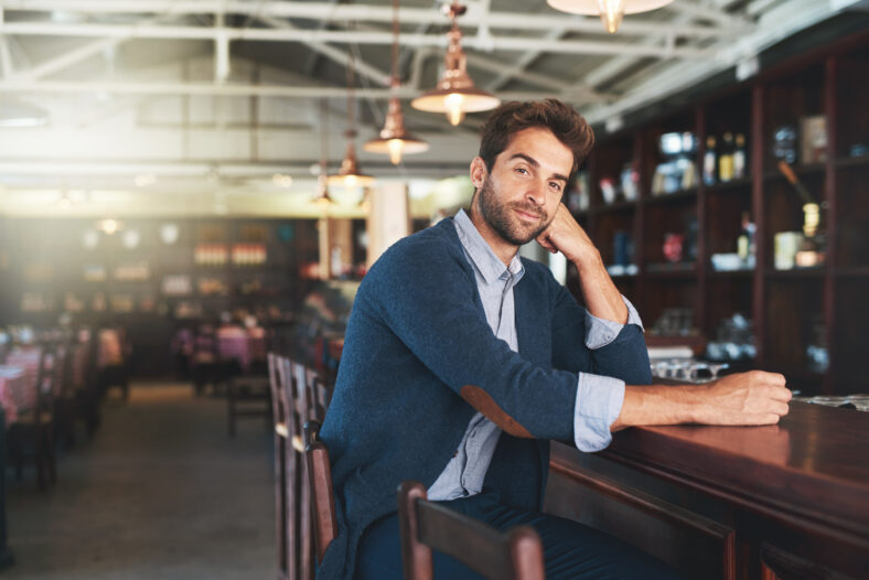 Portrait, relax and business with man, bar and sitting with break and alcohol establishment. Face, person and guy with vacation and peace with entrepreneur and patience with fashion and counter.