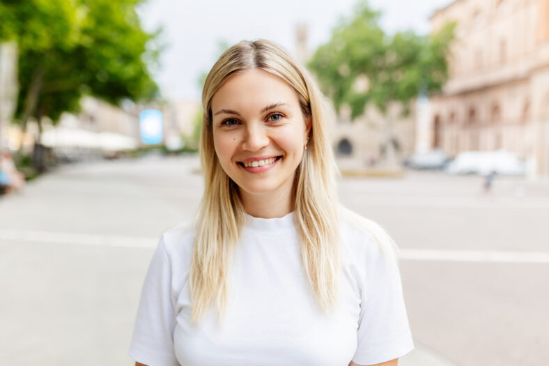 Retrato sonriente de joven caucásica que mira a la cámara de pie en City Street. Chica milenaria alegre que se siente positiva, primer plano de la cabeza al aire libre. Gente feliz