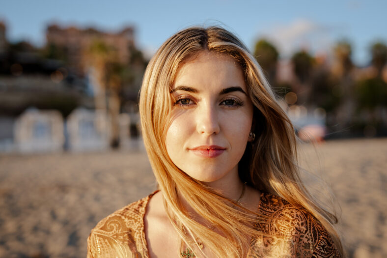 Portrait of one young, beautiful woman on the sand of the beach enjoying and relaxing at the sunset of the day. Looking at the camera serious.