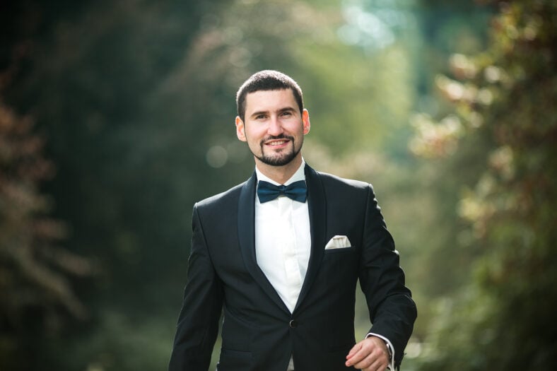 confident groom posing for the camera in the park