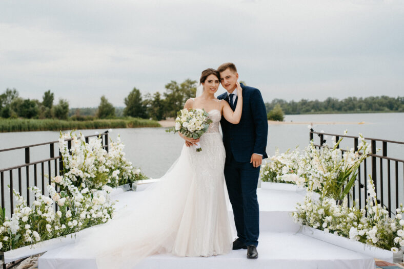 bride and groom against the backdrop of a yellow sunset on a pier near the river