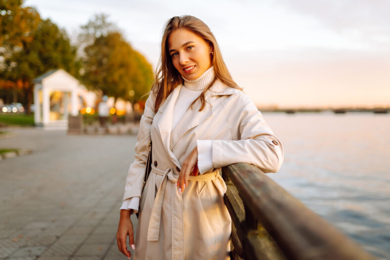 A young woman walks along the embankment and enjoys the warm autumn sunset. Lifestyle, travel, tourism, active life.