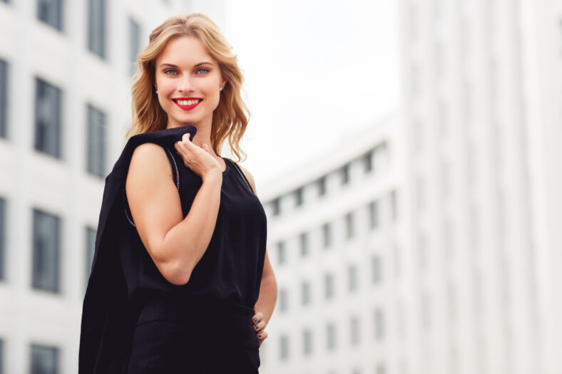 Outdoors portrait of attractive smiling woman with blonde wavy hair on business centre background. Split toned photo