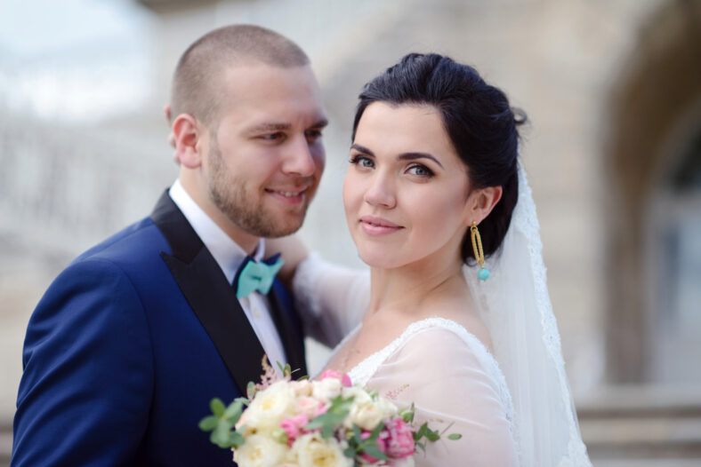 Wedding couple on the nature is hugging each other. Beautiful model girl in white dress. Man in suit. Beauty bride with groom. Female and male portrait. Woman with lace veil. Lady and guy outdoors