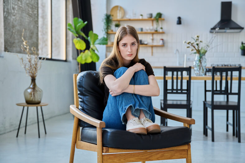 Portrait of young beautiful woman, serious college university student looking at camera sitting at home in chair. Attractive female blonde, lifestyle, youth concept