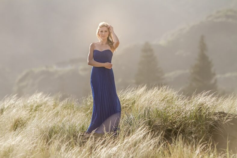 outdoor portrait of young beautiful blonde woman in blue gown posing on natural background