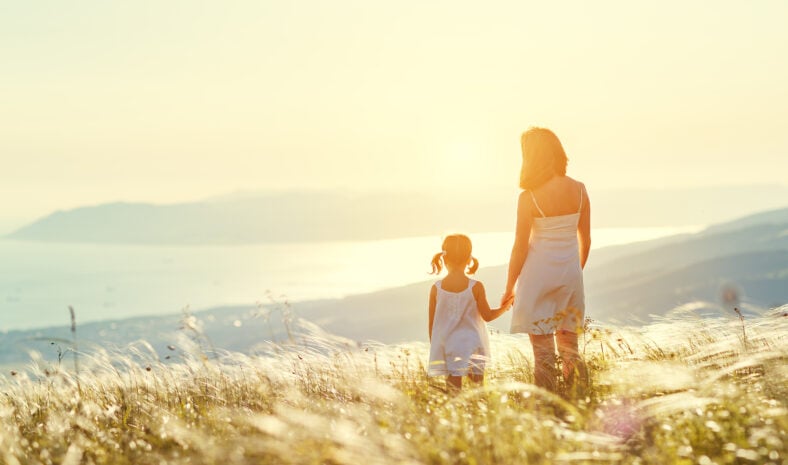 Happy family in summer outdoors. Mother and child daughter stand with their backs and admire sunset