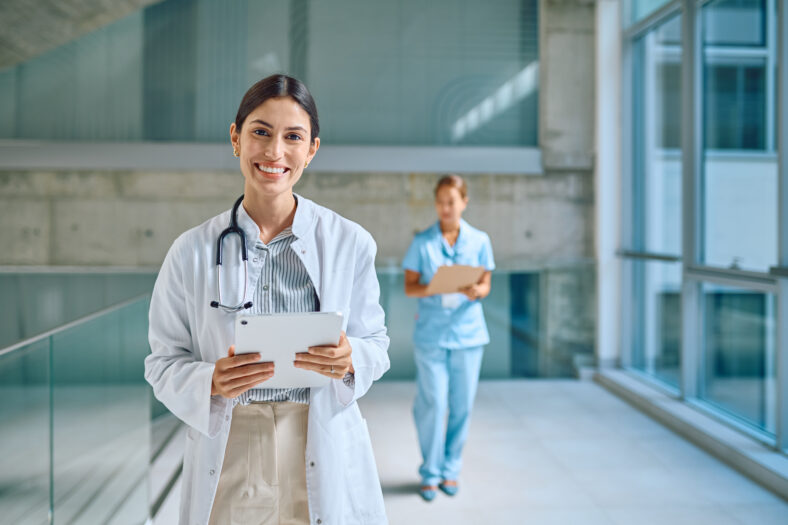 Portrait of smiling female doctor holding tablet in hospital corridor
