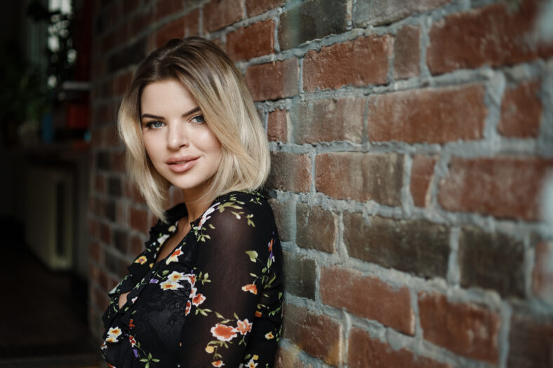 Portrait of a happy woman posing while lying against the wall. Girl standing on the brick wall background