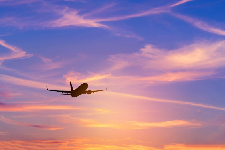 Silhouette passenger airplane flying away in to sky high altitude above the sun during sunset