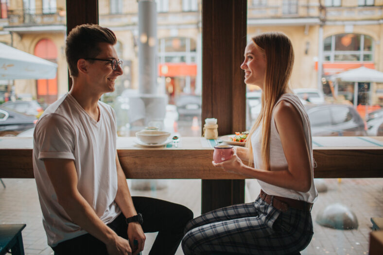 Happy young couple in love having a nice date in a bar or restaurant. They telling some stories about themself , drinking tea or coffee and and eating salad and soup