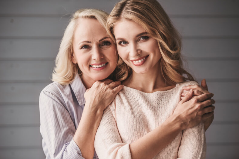 Beautiful senior mom and her adult daughter are hugging, looking at camera and smiling