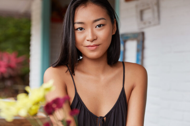 Pleasant looking young Asian woman with attractive appearance, poses indoor in cafeteria, being delighted to spend vacation in unknown country. People, facial expression and lifestyle concept