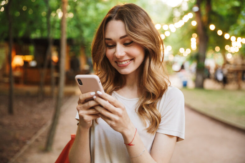 Smiling young girl holding mobile phone while standing at the park
