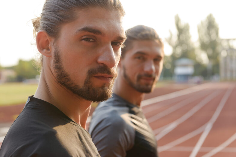 Photo of young two twins sportsmen brothers standing at the stadium outdoors.
