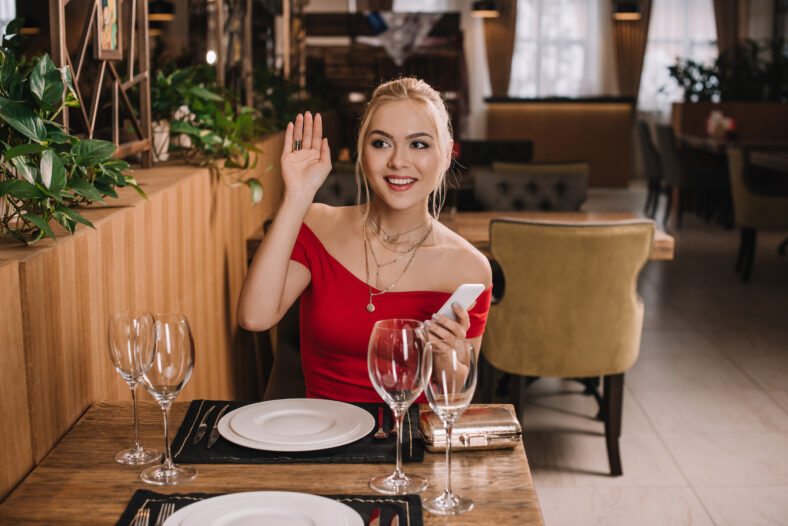 attractive woman in red dress sitting in restaurant waving hand
