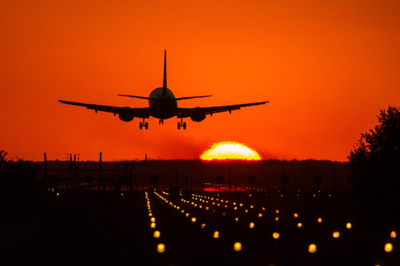 Silhouette of air plane landing on illuminated track at sunset with beautiful red sky and sun in background
