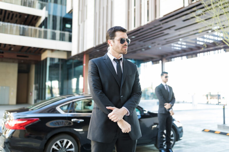 Alert bodyguard keeping an eye on surroundings with car parked on city street