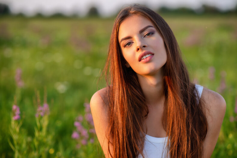 Beautiful girl is on nature on the spring wildflowers background. Beautiful young woman on nature over summer field background. Closeup face. Portrait of a Brunette girl with long brown hair.