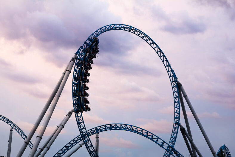 Silhouette of people having fun on a roller-coaster in an amusement park at sunset. Adrenalin concept.
