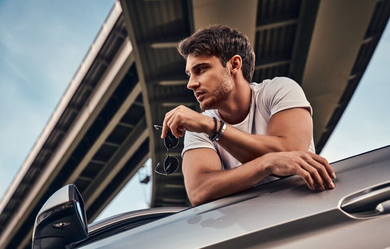 Handsome young man in casual clothes standing near his modern sport car on the street