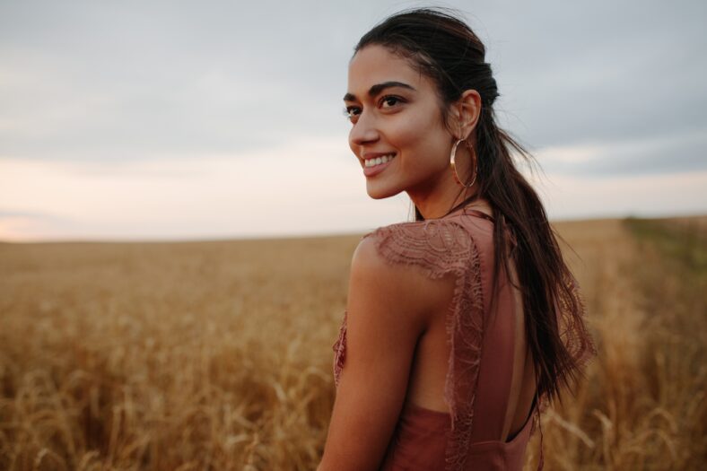 Attractive and carefree woman in the field looking away. Female with a smile in countryside at sunset.