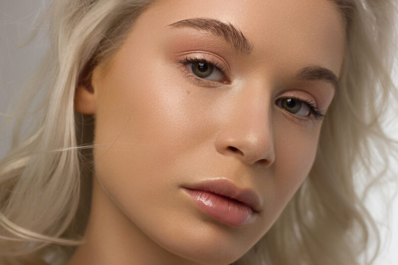 Closeup portrait of a woman with developing curly hair. Sweet tender young blonde girl. Natural lipstick, clear clear skin. Skin care with natural cosmetics in a spa or cosmetology.