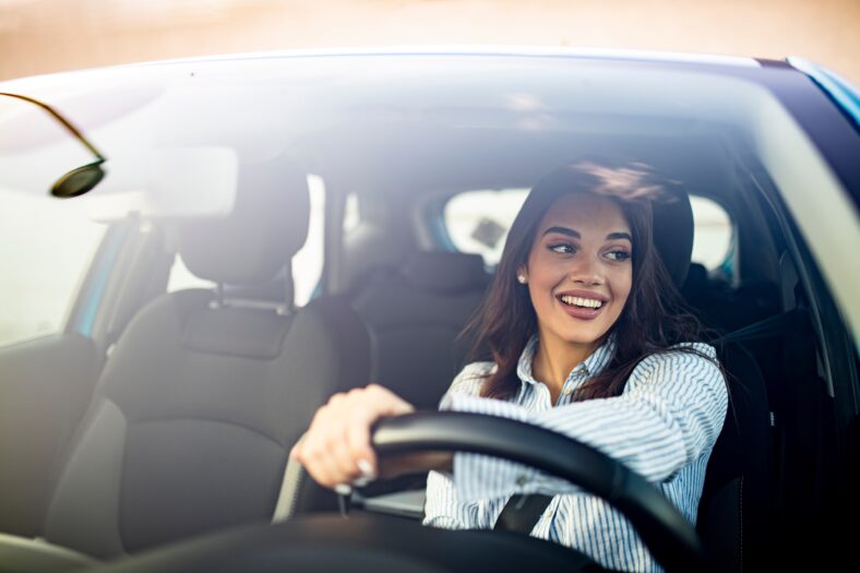 Happy woman driving a car and smiling. Cute young success happy brunette woman is driving a car. Portrait of happy female driver steering car with safety belt