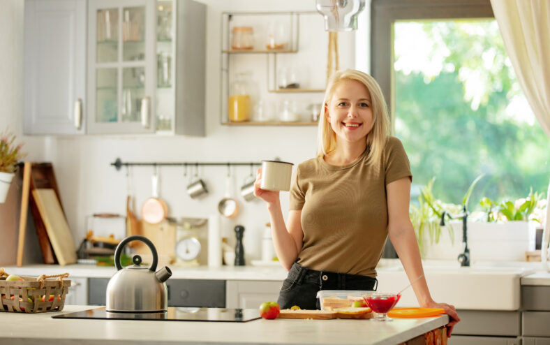blonde woman stands in the kitchen with a cup of coffee