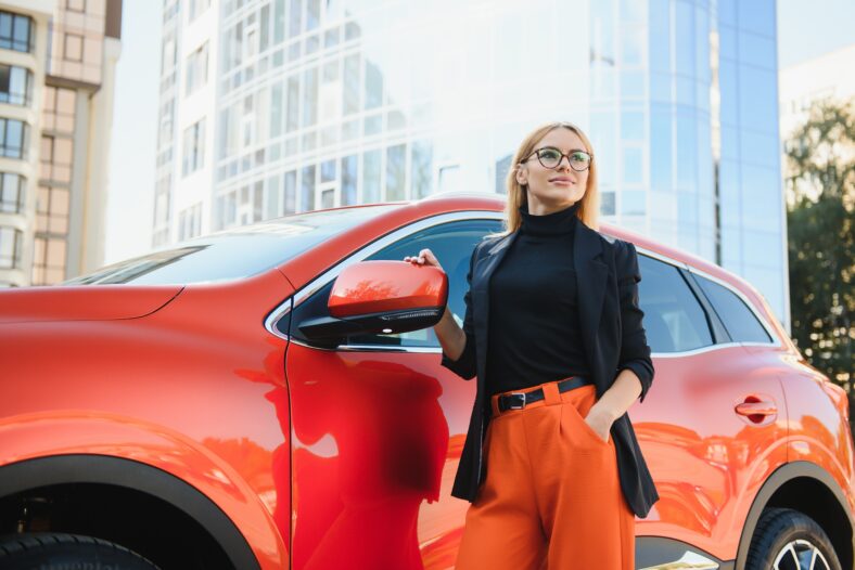 Yong pretty woman standing near a big all terrain car outdoors. Driver girl in casual clothes outside her vehicle.