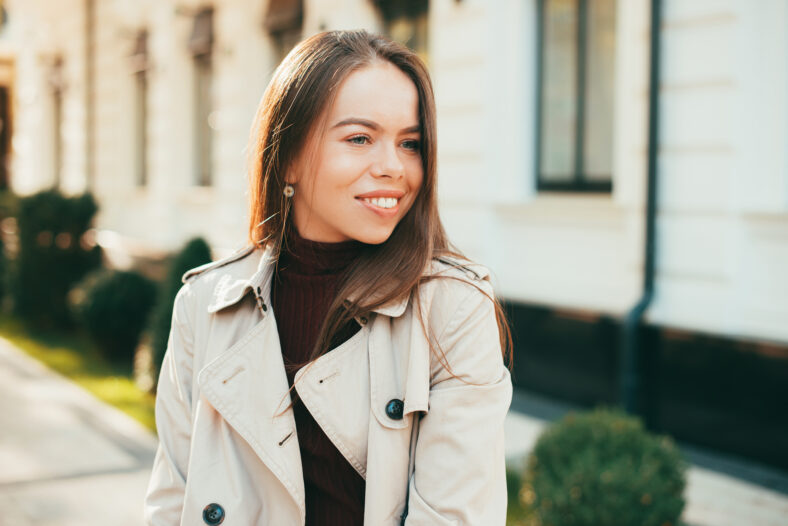 A woman smiling is looking away in a coat on a fall season .