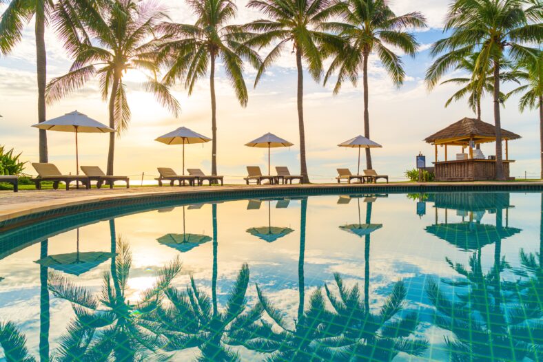 Beautiful luxury umbrella and chair around outdoor swimming pool in hotel and resort with coconut palm tree on sunset or sunrise sky - holiday and vacation concept