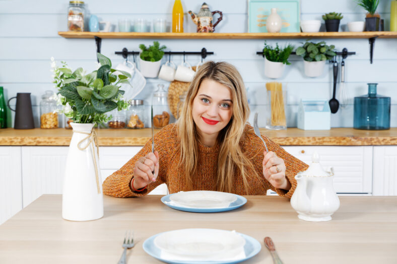 Young attractive woman sitting at table in kitchen with empty plate waiting for lunch