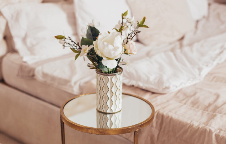 Beautiful bouquet of flowers in vase on bedroom background
