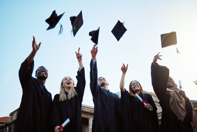 Graduation, education and success with friends in celebration as a graduate group outdoor, throwing mortar caps. Diversity, university and man and woman students celebrating a college diploma.