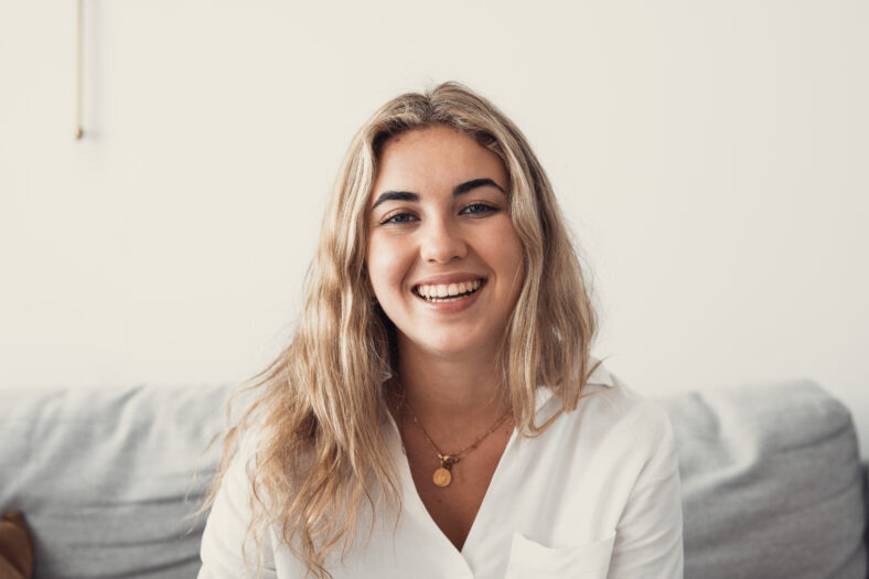 Close up overjoyed woman laughing, sitting on couch at home, head shot portrait young female chatting online with friends or relatives, looking at camera, having fun, making call or shooting video