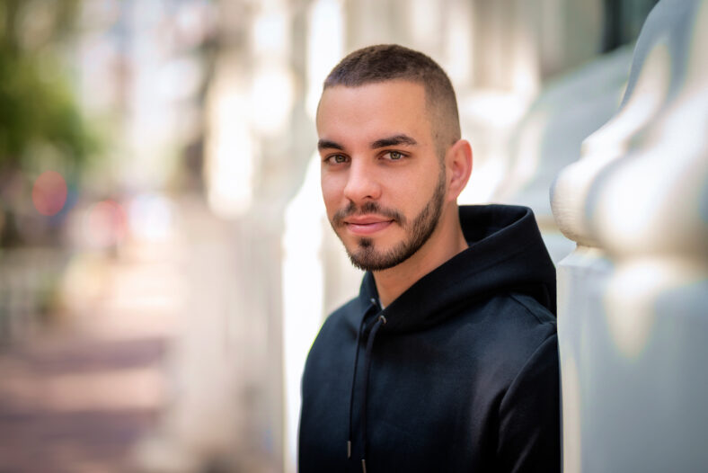 Close-up portrait of a stylish young man standing in a city street. Young male looking at camera and wearing hoodie.