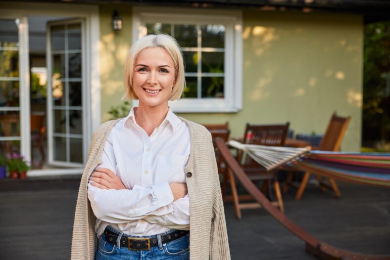 Portrait of happy mature woman standing outside her home backyard patio