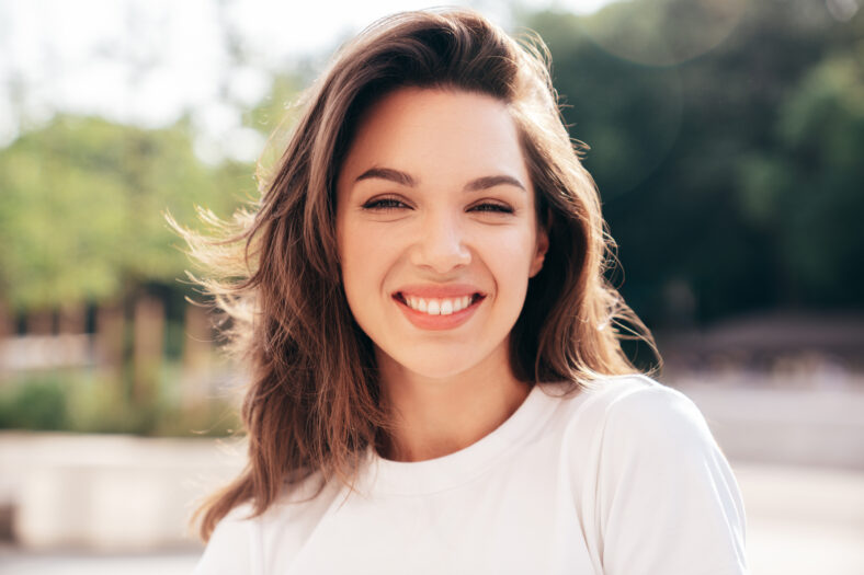 Portrait of young beautiful smiling woman in trendy summer clothes. Sexy carefree woman posing in the street at sunset. Positive model outdoors at sunny day. Cheerful and happy. Closeup