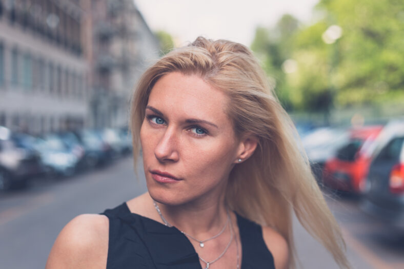Beautiful blonde girl with black minidress and leather jacket posing in the city streets