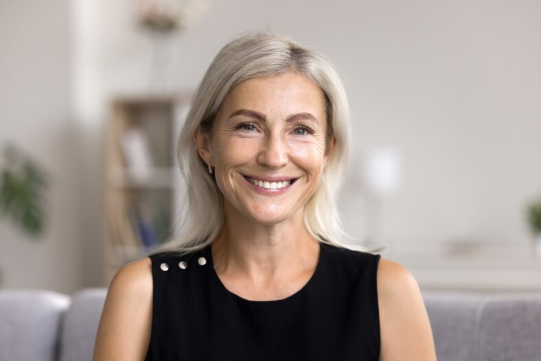 Head shot portrait pretty blonde woman looking at camera, sits alone on sofa photoshooting, enjoy pleasant pastime weekend at home at own or rented apartment. Beautiful mature female profile picture
