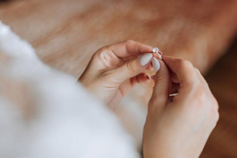 A woman is holding a ring in her hand. The ring is a diamond and it is on her finger